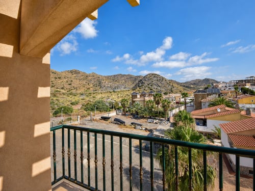 Balcony view from Apartamentos El Calón Playa showing desert hills, palm trees, and village buildings in Cuevas del Almanzora