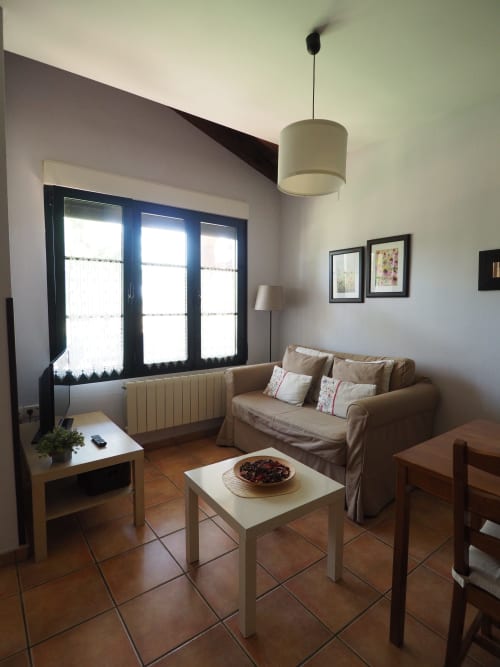 Acogedora sala de estar en los Apartamentos Senda del Duratón con sofá beige, mesa de café y amplias ventanas con vistas a los jardines