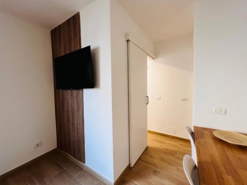 Moderno apartamento con televisor de pantalla plana en pared de madera, área de cocina con mesa de madera y diseño abierto en El