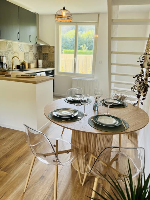 Salle à manger contemporaine du cottage d'Étretat avec table dressée, chaises en bois, cuisine et vue sur le jardin par portes-fenêtres