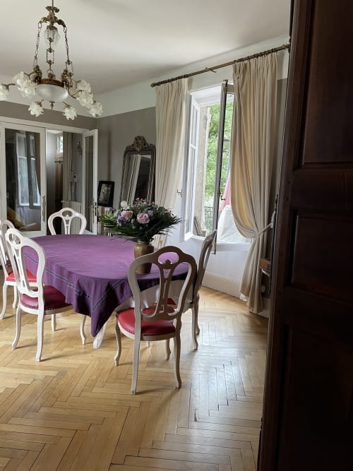Élégante salle à manger de la maison d'hôtes Les Pratges à Figeac avec nappe violette, lustre raffiné et vue sur le jardin