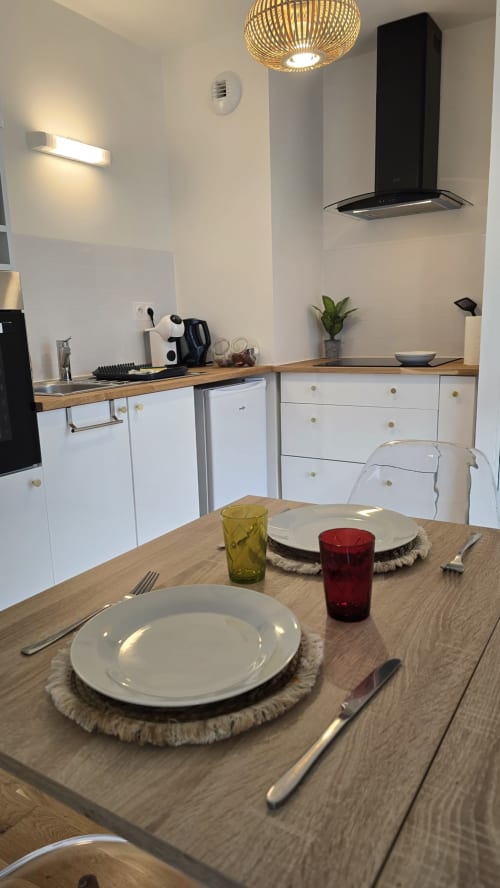 Modern kitchen-dining area at Ô KASTEL apartment in La Fôret-Fouesnant with wooden table, white cabinetry, and black hood