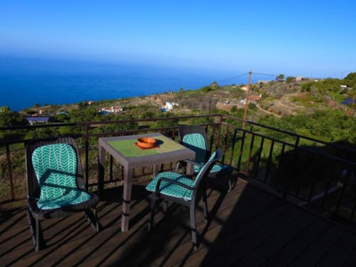 Sillas turquesas con patrón en terraza de Villa Las Flores, con vistas al pueblito de montaña y océano azul en La Palma, España