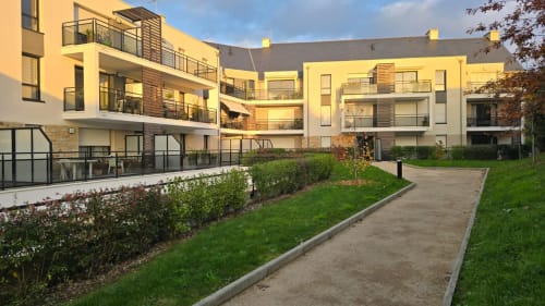 Modern apartment complex in La Fôret-Fouesnant with yellow and white facades, green courtyard, walkways, and contemporary
