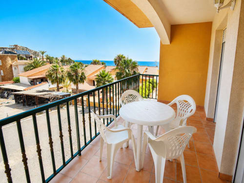 Beachfront apartment balcony with sea views, white furniture, and palm trees at Apartamentos El Calón Playa, Cuevas del