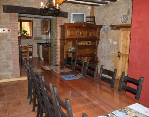 Amplio comedor con mesa de madera, sillas negras, muros de piedra rústica y aparador de madera en Casas Rurales La Viña