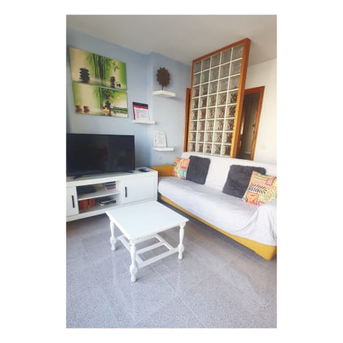 Gemütliches Wohnzimmer in El Médano mit gelbem Bett, TV, weißem Tisch und Meerblick