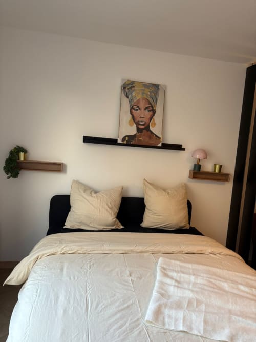 Chambre moderne au Paradis Des Logis avec tête de lit noire, literie crème, oreillers blancs et tableau portrait au mur