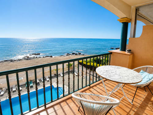 Beachfront apartment balcony with sea view, white table, wicker chairs, and pool at El Calón Playa, Cuevas del Almanzora