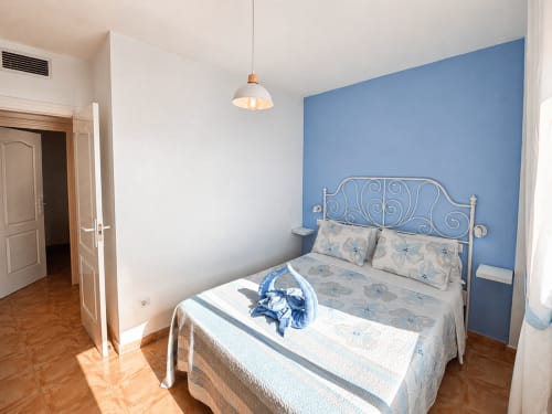 Bedroom with white wrought iron bed, blue accent wall, pendant light at Apartamentos El Calón Playa, Cuevas del Almanzora