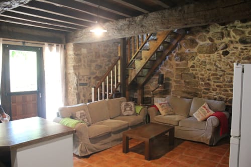 Sala de estar rústica em apartamento de pedra com sofá bege, escadas de madeira e pisos em terracota na Aldeia Rural Santo André, Ourense