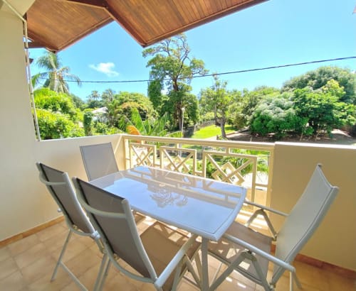 Spacieux balcon avec table à manger et chaises offrant une vue imprenable sur un jardin luxuriant, appartement Maisons En Or à Cayenne