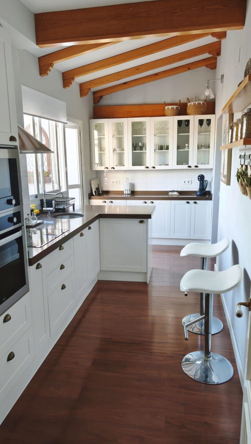 Cocina moderna con armarios blancos, encimeras oscuras, vigas de madera y barra en el apartamento Mirador Medieval de Cáceres