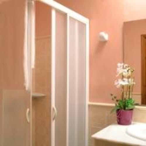 Baño moderno de la villa Las Golondrinas con paredes coralinas, ducha de cristal, orquídea en maceta y elegantes accesorios