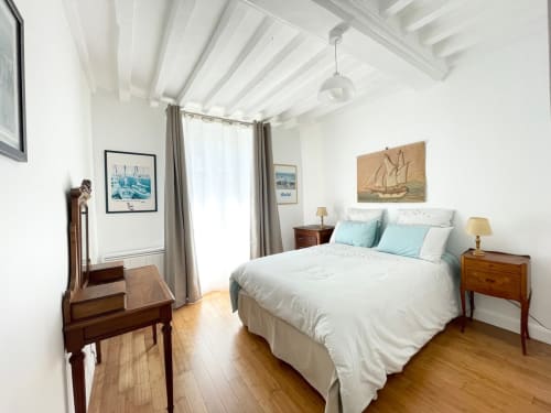 Chambre lumineuse de l'appartement Le 58 Bayeux avec lit queen-size, meubles en bois, décor nautique, poutres apparentes et lumière naturelle