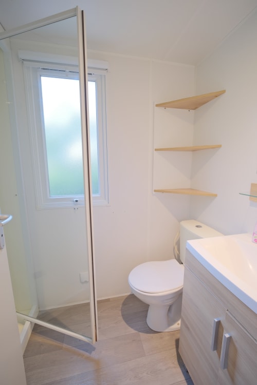 Salle de bain moderne du gîte Annick Mobilhome à Vias Plage avec toilettes, lavabo, étagères en bois et douche