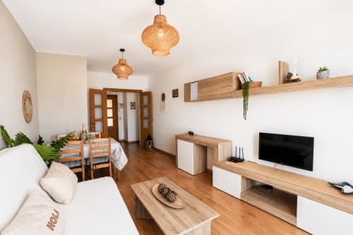 Salon moderne à Corralejo avec meubles en bois, télévision écran plat, luminaires suspendus tissés et balcon vue mer