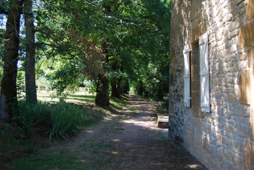 Entrée de gîte en pierre entourée d'arbres aux Pratges B&B à Figeac, France avec allée rustique et jardins verdoyants