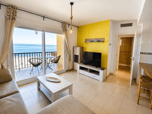 Sala de estar de apartamento frente al mar con pared de acento amarillo, balcón con vista al mar, TV y amueblado moderno en Apartamentos El