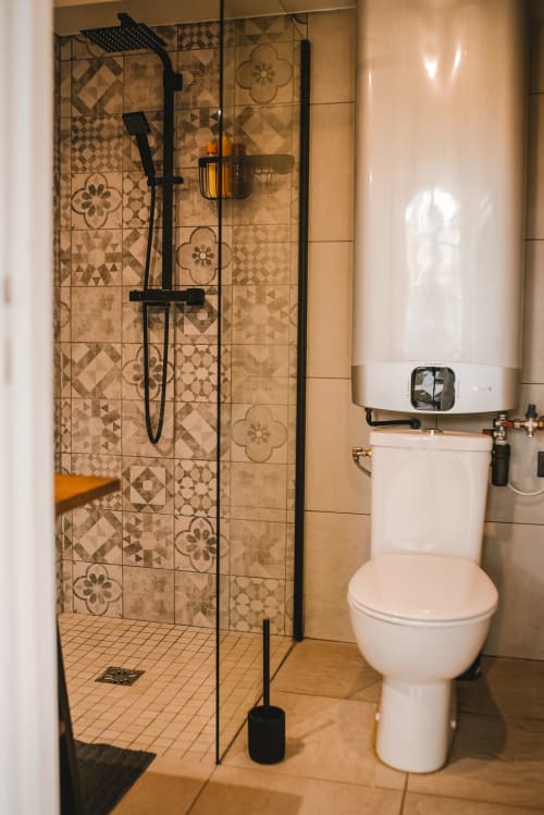 Salle de bain moderne avec douche carrelée décorée, toilettes blanches et robinetterie noire au gîte ART DE VOYAGER à Étretat