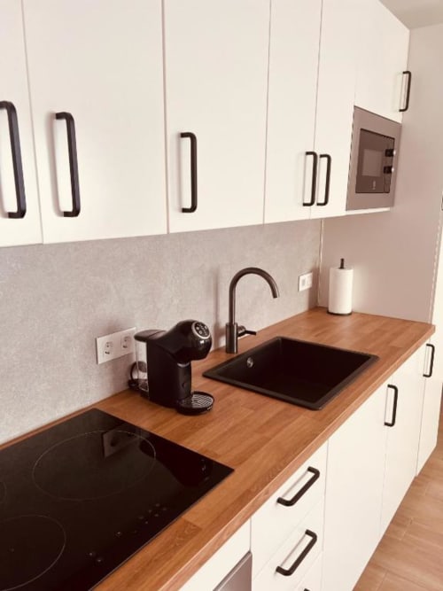 Cocina moderna con gabinetes blancos, encimera de madera, vitrocerámica y fregadero negro en El HierroStay Apartments