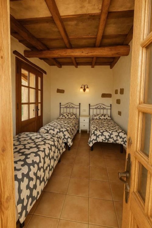 Habitación doble con camas de hierro forjado, vigas de madera vista y suelo de terracota en Villa Awara