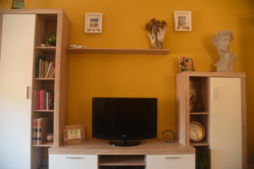 Modern living room in Benavente apartment with flat-screen TV, wooden furniture, and yellow accent wall