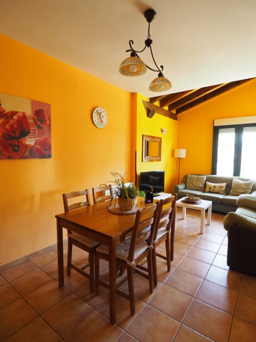 Luminoso comedor y salón en amarillo brillante en apartamento rural español con mesa de madera, sofá de cuero y vistas al jardín