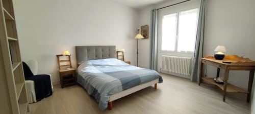 Chambre lumineuse de la villa Mer et Maisons à La Trinité sur Mer avec lit gris capitonné, mobilier en bois et vue sur le jardin