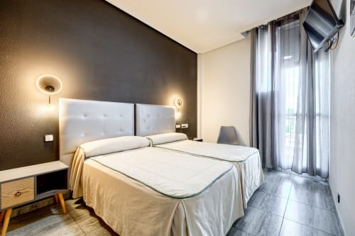 Habitación moderna en Hostal El Molino con dos camas, cabecera blanca, pared oscura de acento y balcón con vistas a las montañas