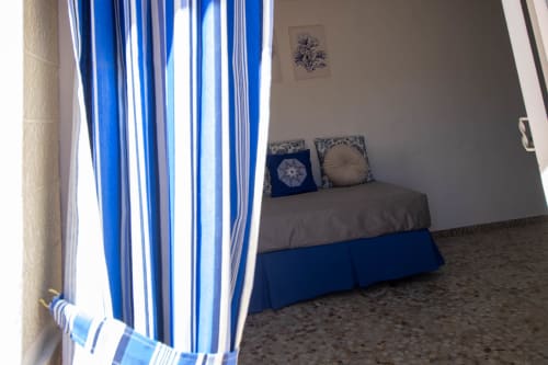 Dormitorio luminoso en La Casa de Tita Clota en Setenil de las Bodegas con cortinas azules a rayas y cama con cojines decorativos