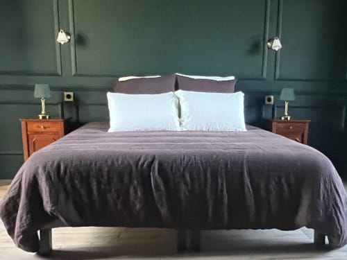 Chambre moderne aux murs vert sauge, literie mauve, oreillers blancs, tables de nuit en bois et luminaires suspendus à La Millière
