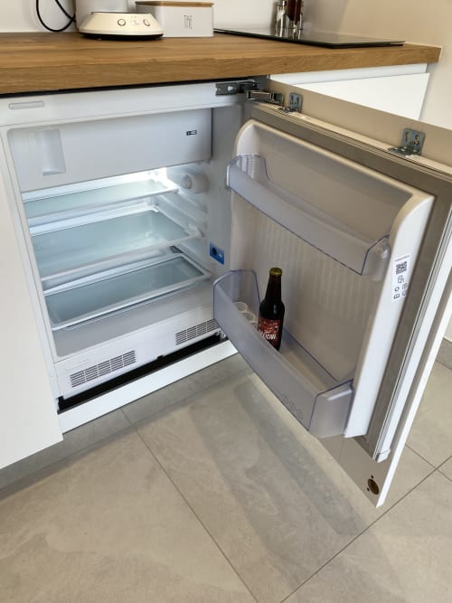 Réfrigérateur ouvert dans l'appartement La Maison Blanche montrant les étagères et une bouteille de bière dans le compartiment de la porte