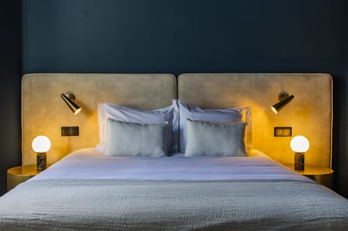 Quarto moderno em hotel do Porto com cabeceira azul, roupa de cama branca, arandelas de leitura em latão e iluminação ambiente aconchegante