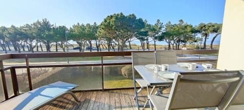 Balcon avec vue mer à Mer et Maisons, La Trinité sur Mer. Chaises longues, table à manger, arbres et front de mer visibles.