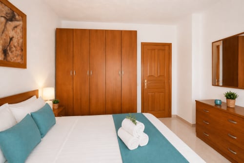 Chambre lumineuse avec armoire en bois, coussins accent bleu-vert et serviettes fraîches à l'appartement Sara & Gino à Fuerteventura