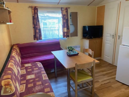 Séjour douillet en mobil-home à Bergerac : canapé-lit, table à manger, télévision et vue jardin par la fenêtre