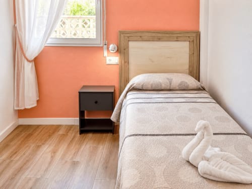 Coral bedroom in Apartamentos El Calón Playa with single bed, wooden headboard, orange accent wall, and sea view window