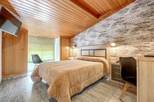 Habitación doble moderna en Hostal El Molino de Collado Villalba con techo de madera, pared de ladrillo y mobiliario contemporáneo