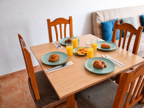 Wooden dining table set with croissants, orange juice, and fresh fruit in Apartamentos El Calón Playa apartment