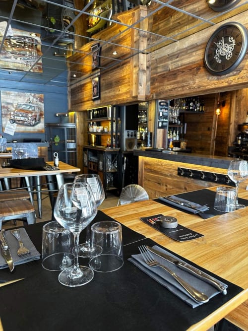 Élégante salle à manger de La Montagnette à Moutiers avec tables en bois, couverts dressés et bar bien approvisionné.