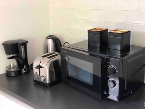 Appareils de cuisine sur le plan de travail : cafetière, bouilloire, grille-pain, micro-ondes et pots de rangement au gîte Art de Voyager