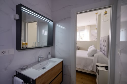 Baño moderno de estudio en Hotel Boutique Alcazaba Salobreña con tocador, espejo iluminado y vista hacia el dormitorio