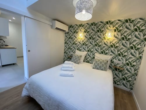 Modern bedroom at La Maison Blanche B&B in Bouguenais with queen bed, green leaf wallpaper, and kitchen area