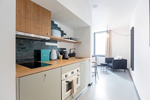 Kitchenette moderna com armários em madeira e backsplash preto em estúdio de hotel no Porto, conectando à área de estar