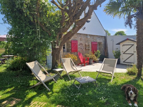 Terrasse de jardin aux Chambres du Keriolet avec chaises longues, maison en pierre, accents rouges et chien à La Trinité sur Mer