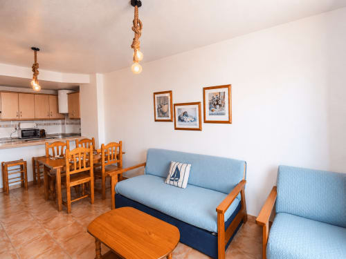 Living room with blue sofas, wooden dining table, and kitchen at Apartamentos El Calón Playa