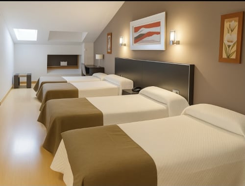 Habitación cuádruple clásica en Hotel Villa de Cacabelos con cuatro camas, servicios modernos e iluminación cálida