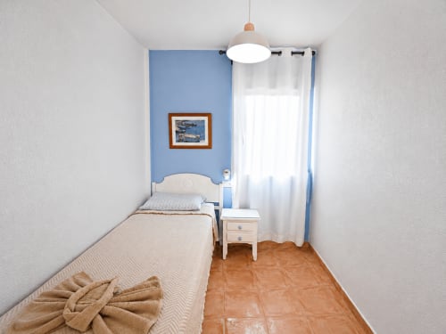 Bright bedroom at Apartamentos El Calón Playa with blue accent wall, single bed, white nightstand, and sea view window in