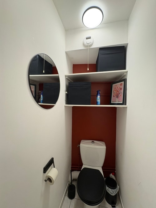 Salle de bain moderne au Paradis Des Logis avec miroir ovale, toilettes blanches, rangements et mur d'accent rouge à Pierrefitte-sur-Seine
